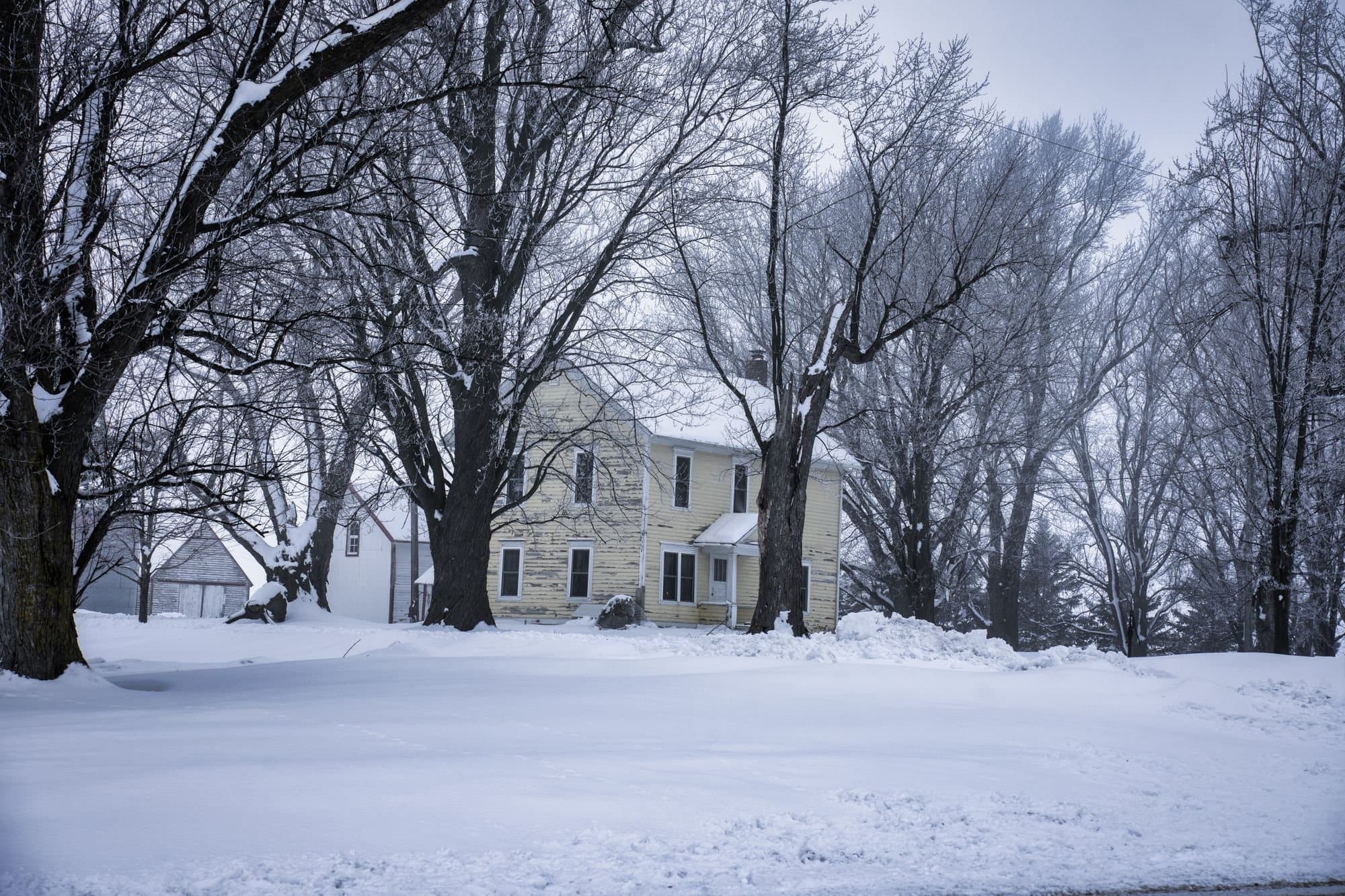 Two-story farmhouse among bare trees after a snowfall